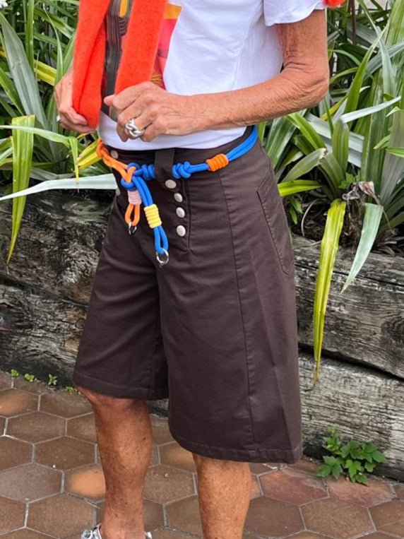 Person standing outdoors with greenery and a paved walkway